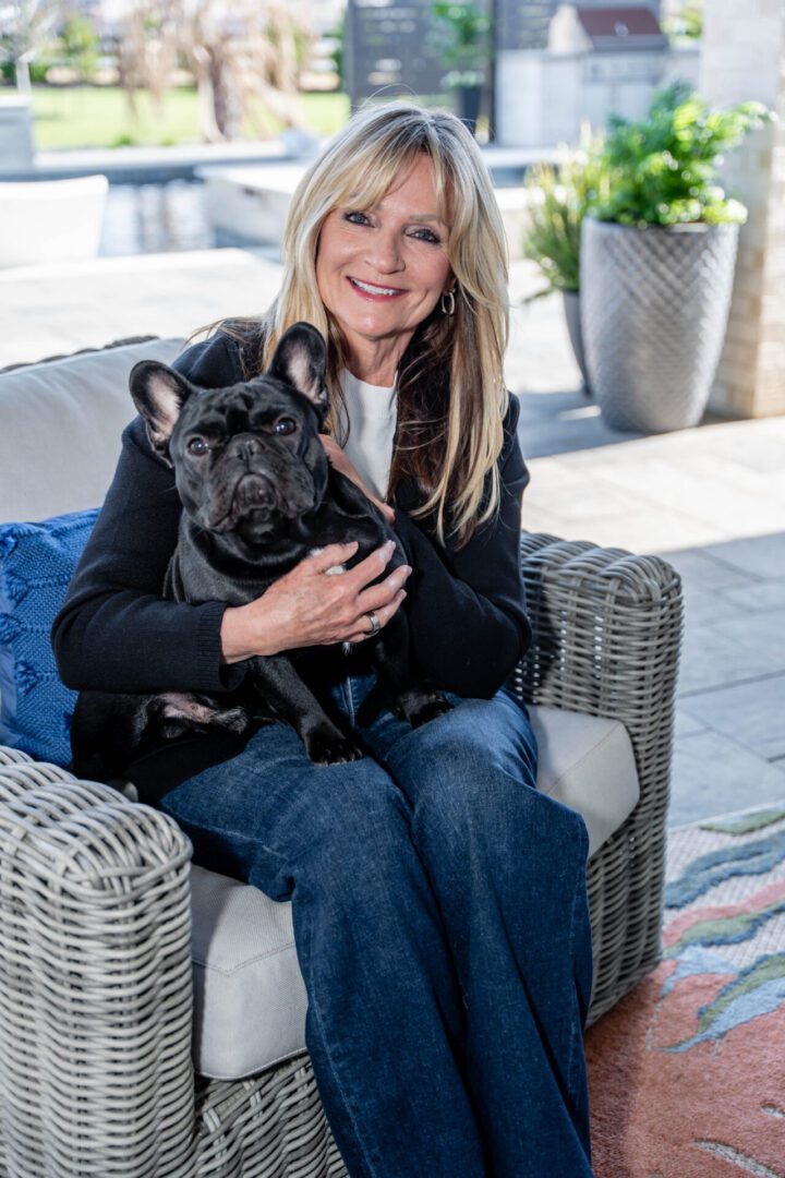 Woman sitting on a wicker chair holding a black French Bulldog.