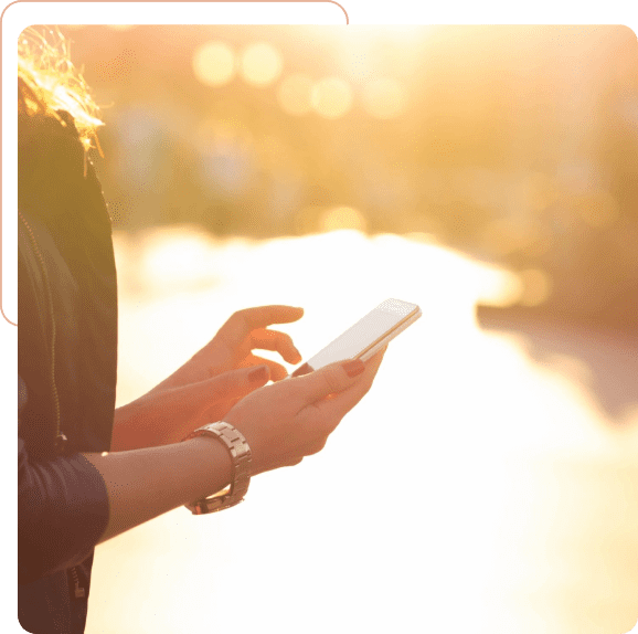Person using smartphone outdoors during golden hour.