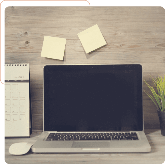 A workspace setup with a laptop, calendar, mouse, sticky notes, and a small plant.